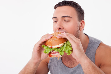 Attractive young man is eating unhealthy hamburger