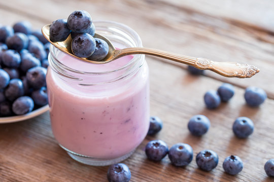 Fresh blueberries yogurt in glass jar, spoon and saucer of bilbe