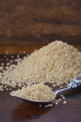 Spoonful of coffee sugar crystals with mound of sugar in background on dark vintage wood background.