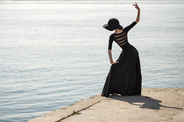 Ballerina in hat and black dress dancing in street.