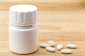 Fototapeta na wymiar White medicine pills bottle on wooden table background