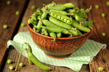 Green peas in a clay bowl on a wooden background