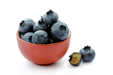 Blueberries in a clay bowl, whole and sliced fruits isolated on