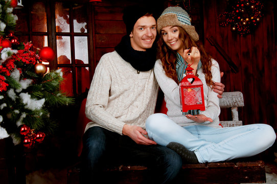 Young couple sitting in the cabin near Christmas tree holding a