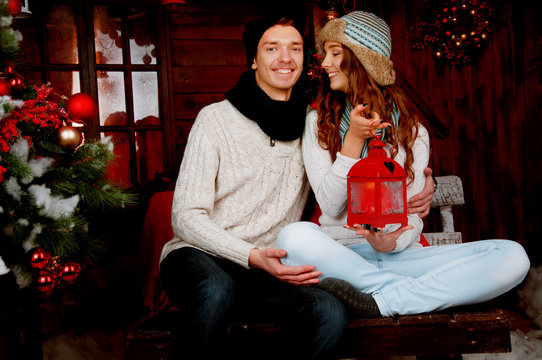 Young couple sitting in the cabin near Christmas tree holding a