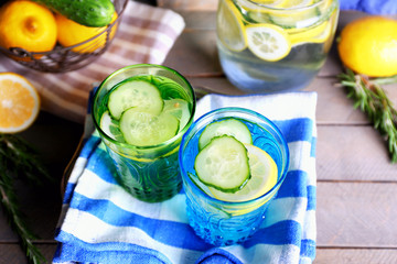 Fresh water with lemon and cucumber in glassware with napkin on wooden table, closeup