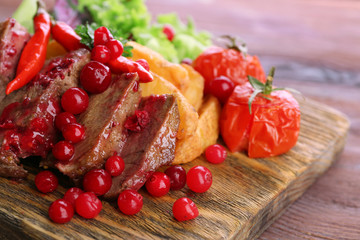 Beef with cranberry sauce, roasted potato slices on cutting board, on wooden background