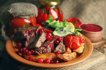 Tasty roasted meat with cranberry sauce, salad and roasted vegetables on plate, on wooden background