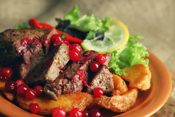 Tasty roasted meat with cranberry sauce, salad and roasted vegetables on plate, on sackcloth background