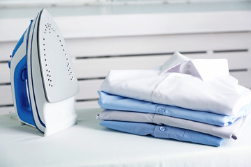 Pile of clothes and electric iron on wooden background