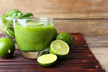 Glass of green healthy juice with basil and limes on table close up