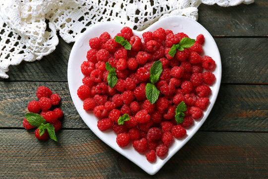Sweet raspberries on plate, on wooden  background