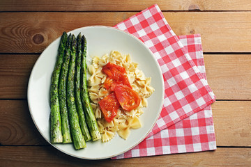 Roasted asparagus and tasty pasta with vegetables on plate on wooden table background