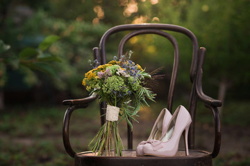 Beautiful wedding shoes with high heels and a bouquet of colorful flowers on a vintage chair on the nature in sunset light, decorations, preparing for the wedding, details, boudoir