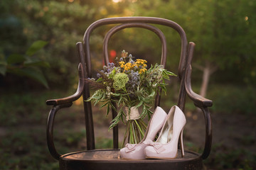 Beautiful wedding shoes with high heels and a bouquet of colorful flowers on a vintage chair on the...