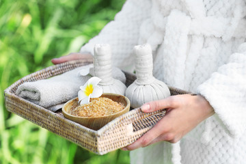Woman in bathrobe holding wicker tray with spa products on river