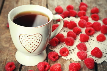 Fresh raspberries with cup of tea on wooden table with napkin, closeup