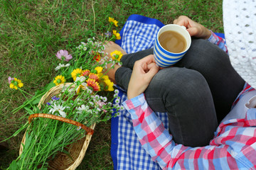 Young woman with cup of coffee sitting on meadow outdoors