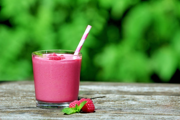 Glass of raspberry milk shake with berries on bright background