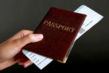 Female hand holding passport and ticket on dark background