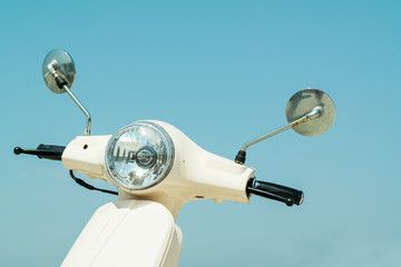 Naklejka premium Detail of classic off-white scooter with headlight, handlebar and mirrors against blue sky