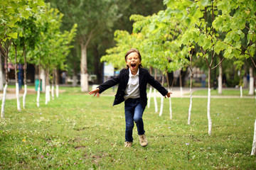 Happy little brunette boy runs in a summer park