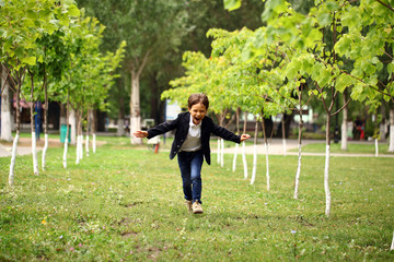 Fototapeta premium Happy little brunette boy runs in a summer park