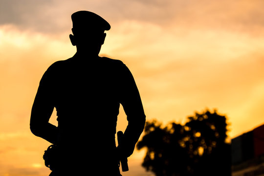 Silhouette of police standing on sunset background.