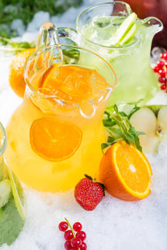 a mix of several bright colored delicious cold lemonade carafes of cucumber and orange and basilon with creative composition