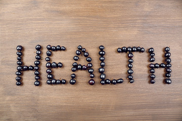 Word HEALTH made of black currant on wooden background