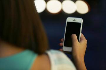 Female hand with mobile phone on blurred night lights background