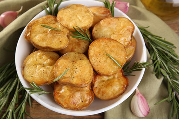 Delicious baked potato with rosemary in bowl on table close up