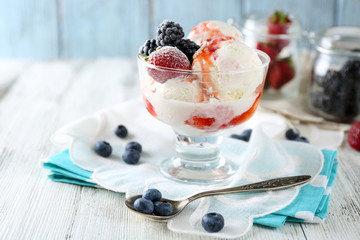 Delicious ice cream with fresh frozen berries and sauce, on color wooden background