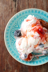Delicious ice cream with fresh frozen berries and sauce, on wooden background