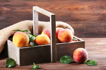 Fresh peaches in crate with sackcloth on wooden background