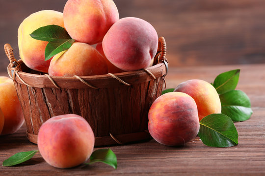 Fresh peaches in wicker basket on wooden table, closeup