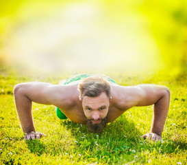 Sports man with brown hair and a beard on a natural background, performing push-ups