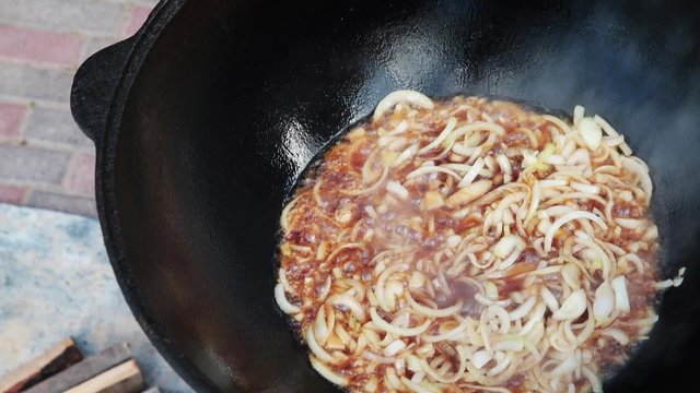 Uzbek national dish pilaf in a large cast-iron cauldron on the fire, fry the chopped onion until golden brown, lamb, carrot, mutton fat, the fat tail, sesame oil, garlic