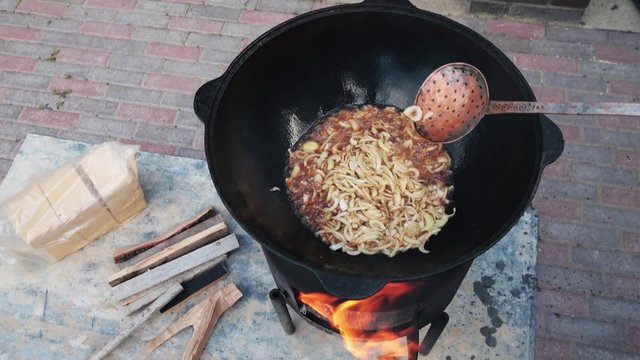 Uzbek national dish pilaf in a large cast-iron cauldron on the fire, fry the chopped onion until golden brown, lamb, carrot, mutton fat, the fat tail, sesame oil, garlic
