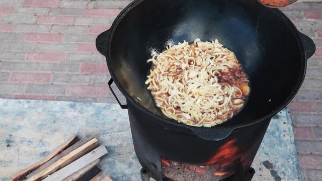 Uzbek national dish pilaf in a large cast-iron cauldron on the fire, fry the chopped onion until golden brown, lamb, carrot, mutton fat, the fat tail, sesame oil, garlic