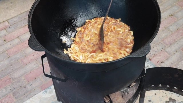 Uzbek national dish pilaf in a large cast-iron cauldron on the fire, fry the chopped onion until golden brown, lamb, carrot, mutton fat, the fat tail, sesame oil, garlic