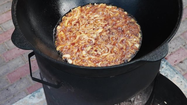 Uzbek national dish pilaf in a large cast-iron cauldron on the fire, fry the chopped onion until golden brown, lamb, carrot, mutton fat, the fat tail, sesame oil, garlic
