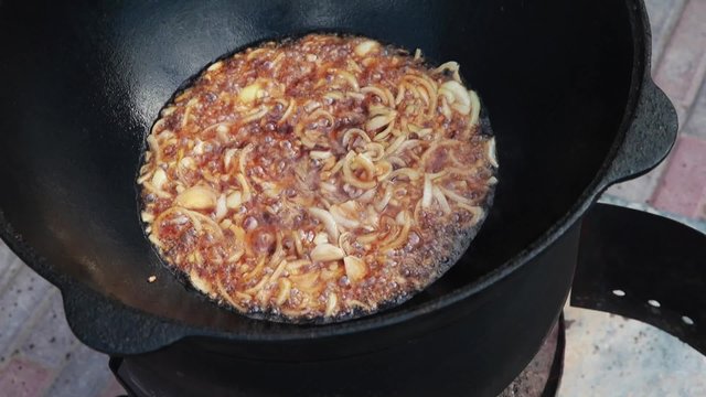 Uzbek national dish pilaf in a large cast-iron cauldron on the fire, fry the chopped onion until golden brown, lamb, carrot, mutton fat, the fat tail, sesame oil, garlic