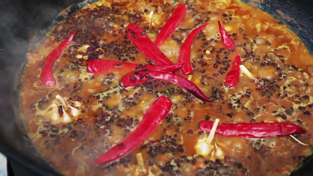 Uzbek national dish pilaf in a large cast-iron cauldron on the fire, sliced red carrots, added barberry, whole of garlic and red chili pepper, boiling, rice, lamb, mutton fat, the fat tail, sesame oil