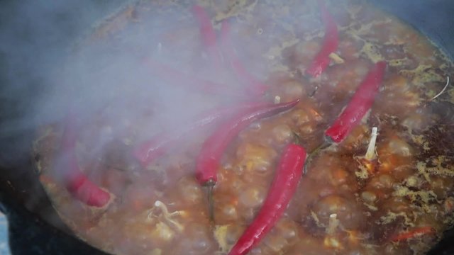 Uzbek national dish pilaf in a large cast-iron cauldron on the fire, sliced red carrots, cold water, add whole of garlic and red chili pepper, boiling, rice, lamb, mutton fat, the fat tail, sesame oil