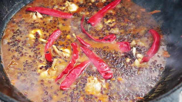 Uzbek national dish pilaf in a large cast-iron cauldron on the fire, sliced red carrots, added barberry, whole of garlic and red chili pepper, boiling, rice, lamb, mutton fat, the fat tail, sesame oil
