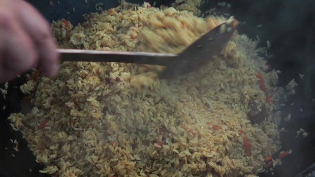 Uzbek national dish pilaf in a large cast-iron cauldron on the fire, mixed ready pilaf, sliced red carrot, barberry, garlic wholes, red chili pepper, rice, lamb, mutton fat, the fat tail, sesame oil