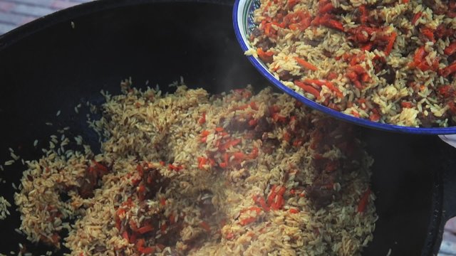 Uzbek national dish pilaf in a large cast-iron cauldron on the fire, spread pilaf on a large plate, carrot, barberry, garlic wholes, red chili pepper, rice, lamb, mutton fat, the fat tail, sesame oil