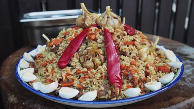 Uzbek national dish pilaf in a large cast-iron cauldron on the fire, on a plate with pilau spread red chili, garlic, quail eggs, carrot, barberry, rice, lamb, mutton fat, the fat tail, sesame oil