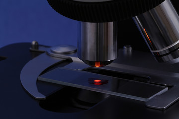 The red drop of a red liquid like blood  illuminated from below by condenser  on a slide of a dark (obscured) microscope. Focus on a slide and objectives. 